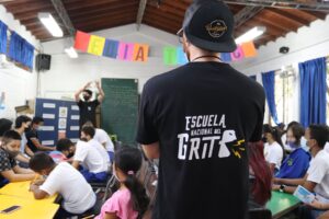 Persona con la camiseta de la Escuela Nacional del Grito, de espaldas, en un taller en un colegio